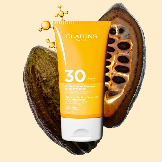 Photo de la Crème Solaire Jeunesse Haute Protection SPF 30 Clarins pour le corps, parmi des molécules de collagène et des fèves de cacao.