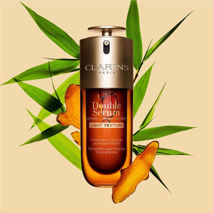 Een flacon Clarins Double Serum Light Texture van 50 ml tussen kurkuma en Proven&ccedil;aals pijlriet tegen een oranje achtergrond.