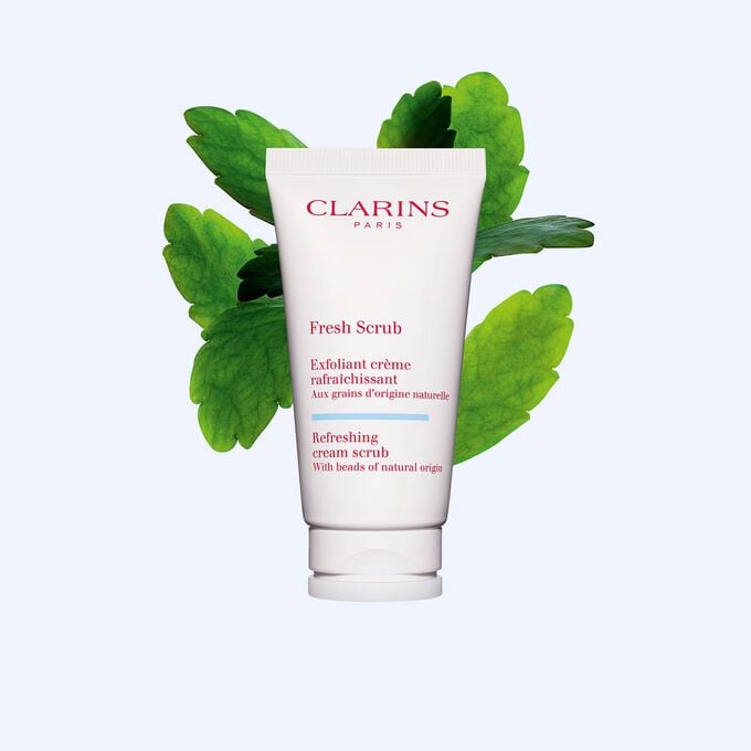 Packshot van de tube van de Clarins Fresh Scrub gezichtsscrub naast enkele kalancho&euml;-bladeren tegen een witte achtergrond.