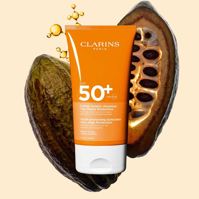 Afbeelding van Clarins Youth-protecting Sunscreen Very High Protection SPF 50+ voor het lichaam tussen collageenmoleculen en cacaobonen.