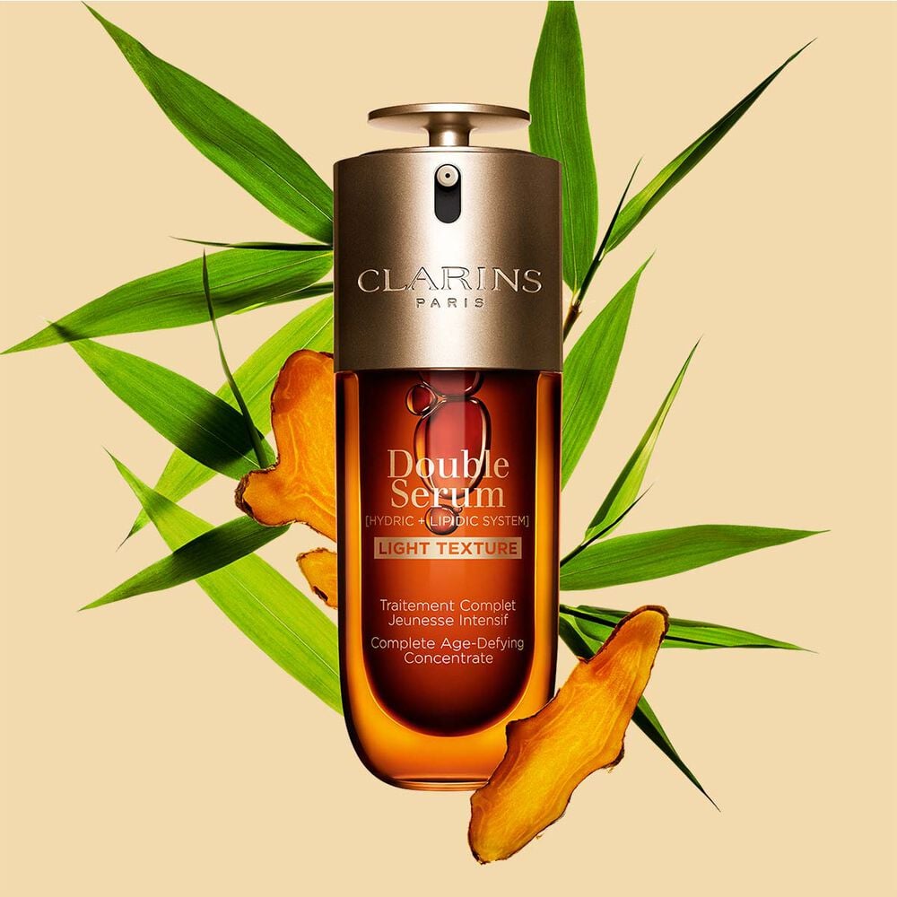 Een flacon Clarins Double Serum Light Texture van 70 ml tussen kurkuma en Proven&ccedil;aals pijlriet tegen een oranje achtergrond.