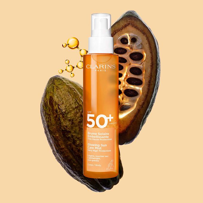 Plan produit de la Brume Solaire Embellissante SPF 50+ Clarins, un spray invisible, devant une mol&eacute;cule de collag&egrave;ne et des f&egrave;ves de cacao.