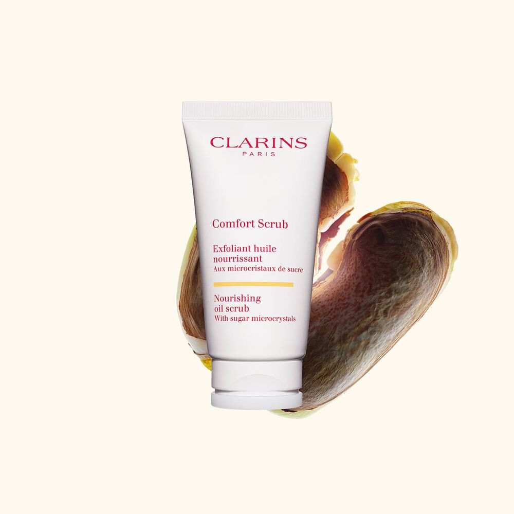 Packshot van de Clarins Comfort Scrub tube voor het gezicht en de lippen naast enkele wilde mangopitten tegen een beige achtergrond
