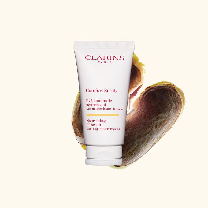 Packshot van de Clarins Comfort Scrub tube voor het gezicht en de lippen naast enkele wilde mangopitten tegen een beige achtergrond